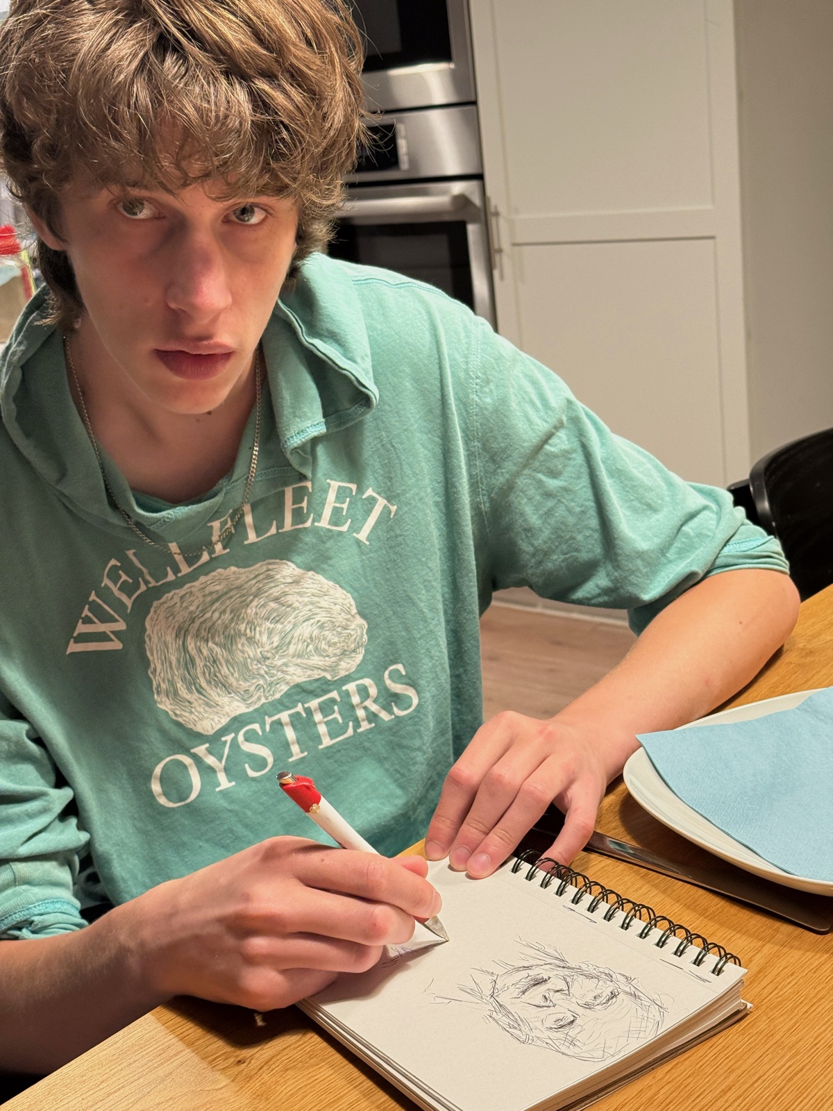 Jeremy at a kitchen table, drawing a face in a sketchbook