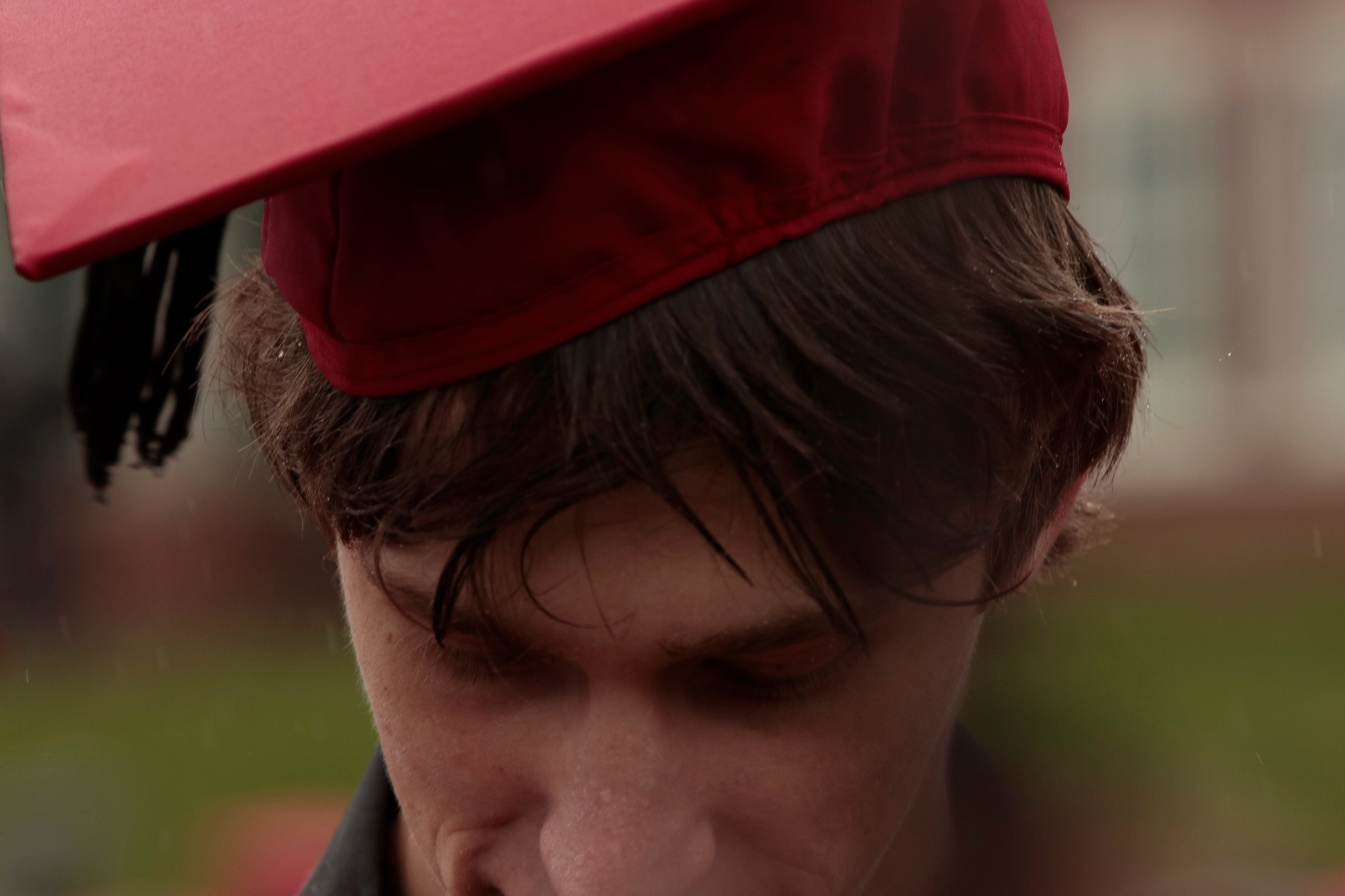 Jeremy Zay in a red graduation cap, looking down